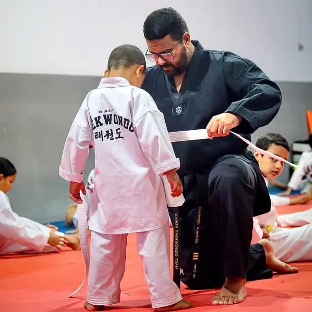 Mestre da Black Belt Foundation ajusta a faixa de um jovem atleta no DOJAN